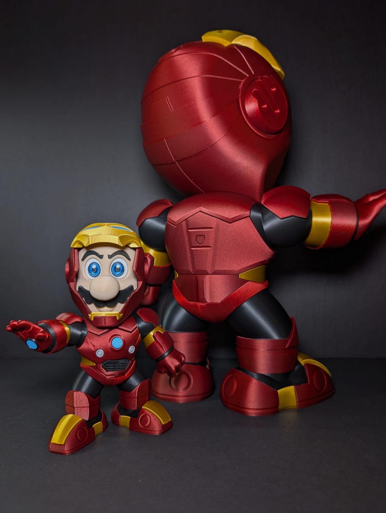 May include: Two red and gold action figures, one large and one small, resembling a mashup of Mario and Iron Man. The figures have a metallic finish, with black accents and yellow highlights. The smaller figure is in front of the larger one.