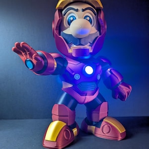 May include: A 3D-printed figurine of Mario in an Iron Man suit. The figure is primarily red and gold, with blue accents and glowing lights. The helmet and boots are gold, while the body is red. The figure is posed with one arm outstretched.
