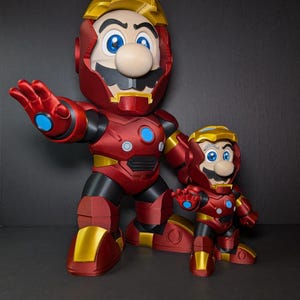 May include: Two figurines of Mario in Iron Man armor. The larger figure is red and gold with blue accents, and the smaller figure has the same design. Both figures have Mario's signature mustache and blue eyes.