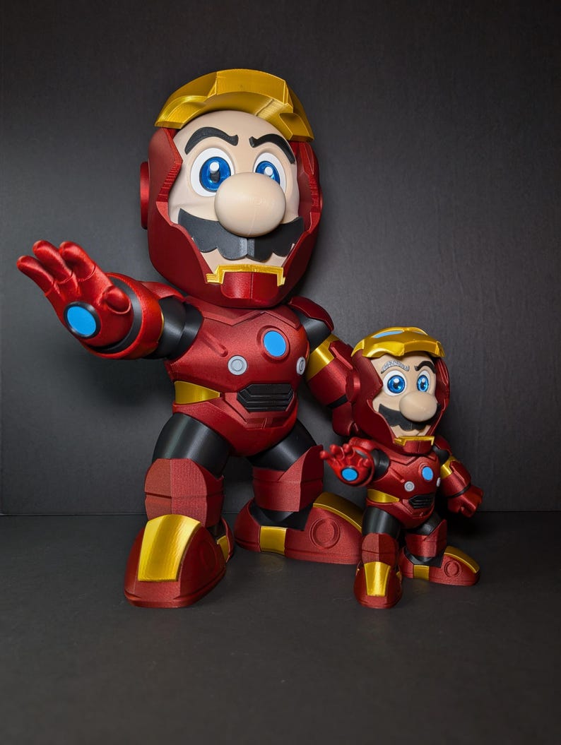 May include: Two figurines of Mario in Iron Man armor. The larger figure is red and gold with blue accents, and the smaller figure has the same design. Both figures have Mario's signature mustache and blue eyes.