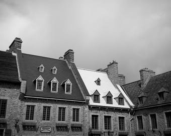 Könnte beinhalten: Schwarz-Weiß-Foto von historischen Gebäuden mit Steinfassaden und steilen Dächern. Dachgauben und Schornsteine sind zu sehen. Der Himmel ist bewölkt.