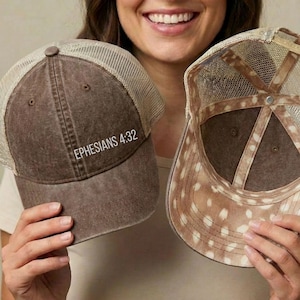 May include: Two trucker hats with a distressed brown finish and beige mesh back panels. One hat displays the white text EPHESIANS 4:32 on the front panel. The other hat is shown from the interior, revealing a brown and white spotted pattern.