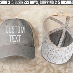 May include: A grey trucker hat with a mesh back and the words CUSTOM TEXT embroidered in white on the front. The interior of the hat features a white lining with a black polka dot pattern, and an adjustable snapback closure is visible at the back.