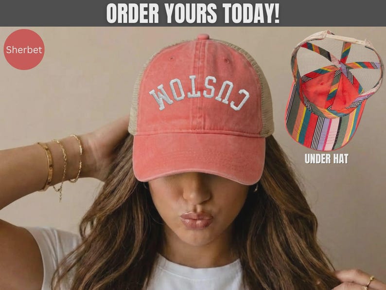 May include: A sherbet-colored baseball cap with a mesh back and the word CUSTOM embroidered in white on the front. An inset shows the underside of the hat, which features a colorful vertical striped pattern and a crisscross strap design.