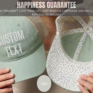 May include: A sage green trucker hat with a mesh back and white embroidered text that reads CUSTOM TEXT. The interior of the hat features a white lining with a black polka dot pattern. The hat has a structured front panel and a curved brim.