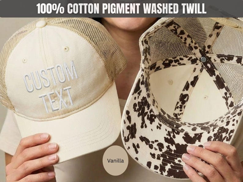May include: A vanilla-colored trucker hat made of 100% cotton pigment washed twill. The front panel features the embroidered text CUSTOM TEXT in white. The hat has a mesh back and an interior lining with a brown and white cow print pattern.