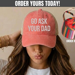 K&ouml;nnte beinhalten: Korallenfarbene Trucker-M&uuml;tze mit dem Text "GO ASK YOUR DAD" in Wei&szlig;. Die M&uuml;tze hat einen Mesh-R&uuml;cken und einen gebogenen Schirm. Das Bild zeigt auch eine bunt gestreifte Unterkappe.