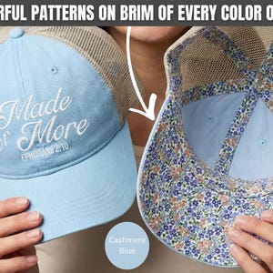 May include: A light blue trucker hat with a tan mesh back. The front features white embroidered text reading Made for More EPHESIANS 2:10. The interior of the brim and the inner seams are lined with a colorful floral pattern of blue and peach flowers.