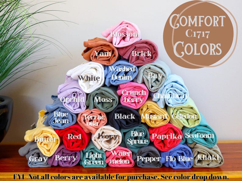 May include: A pyramid of rolled Comfort Colors C1717 t-shirts in various shades including blossom, yam, brick, white, washed denim, bay, orchid, moss, crunchberry, chambray, blue jean, terracotta, black, mustard, celedon, butter, red, ivory, blue spruce, paprika, seafoam, gray, berry, light green, watermelon, pepper, flo blue, and khaki.
