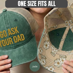 K&ouml;nnte beinhalten: Jadefarbene Trucker-Cap mit dem goldfarbenen Text "GO ASK YOUR DAD". Die Kappe hat einen Mesh-R&uuml;cken und ein Innenfutter mit G&auml;nsebl&uuml;mchenmuster. Der Text "ONE SIZE FITS ALL" befindet sich dar&uuml;ber.