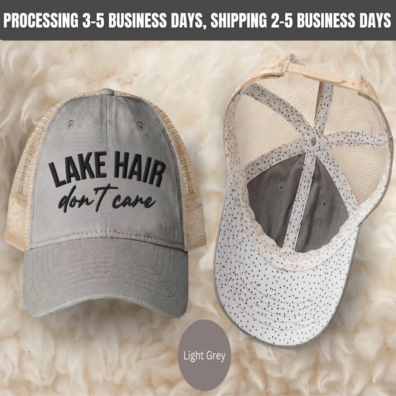 May include: A light grey trucker hat featuring the embroidered black text LAKE HAIR don't care on the front panel. The hat has a mesh back and a curved brim with a white and black polka dot pattern on the underside of the brim and interior.