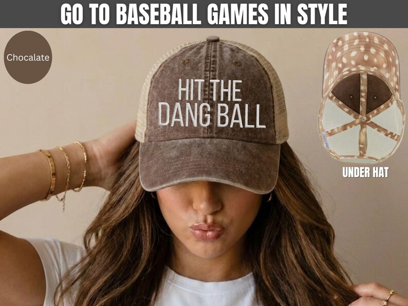May include: A chocolate brown baseball cap with a mesh back and the white embroidered text HIT THE DANG BALL on the front. The hat features a distressed finish and a light brown interior lining with a white polka dot pattern visible in the inset.