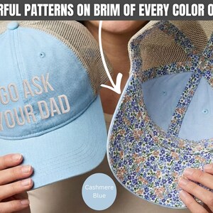 K&ouml;nnte beinhalten: Hellblaue Trucker-Cap mit dem Text "GO ASK YOUR DAD" in Wei&szlig; gestickt. Die Cap hat eine Mesh-R&uuml;ckseite und einen floral gemusterten Rand. Die Farbe ist mit "Cashmere Blue" gekennzeichnet.