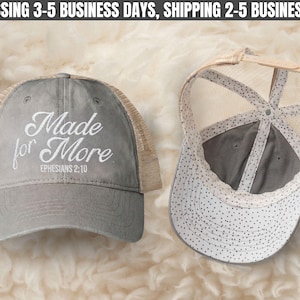 May include: A grey trucker hat with a tan mesh back and an adjustable strap. The front features white embroidered text that reads Made for More EPHESIANS 2:10. The interior lining of the cap displays a white fabric with a black polka dot pattern.