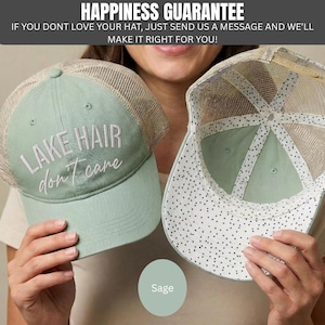 May include: A sage green trucker hat with a mesh back and the embroidered white text "LAKE HAIR don't care" on the front. The interior of the hat features a white lining with a black polka dot pattern and a sage green brim.