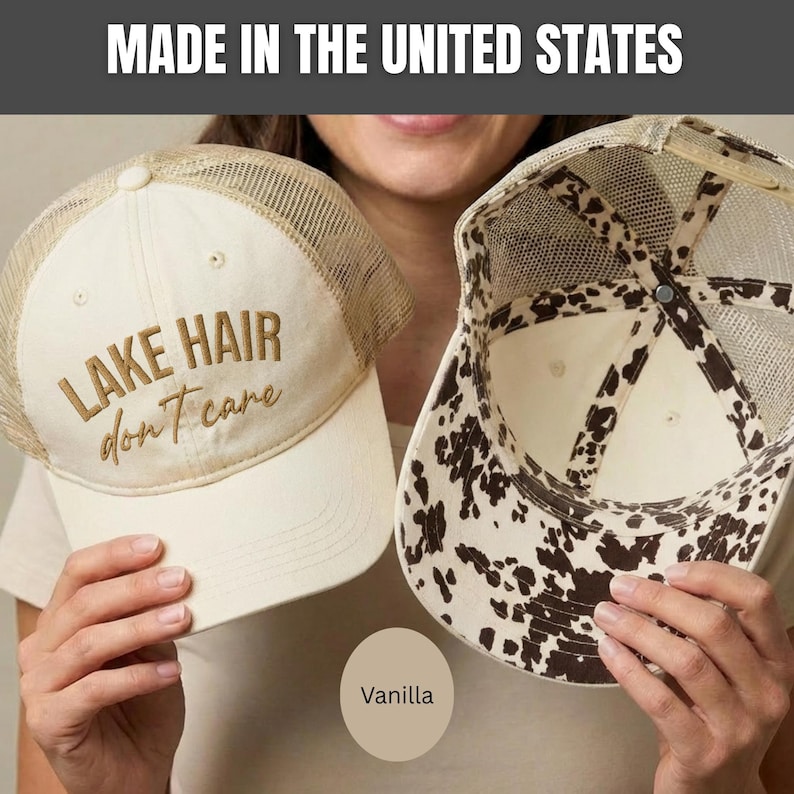 May include: Two trucker hats with mesh backs. One hat is cream-colored with the embroidered brown text 'LAKE HAIR don't care' on the front. The other hat shows the interior, featuring a brown and white cow print pattern on the underside of the brim.