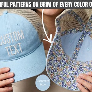 May include: A light blue trucker hat with a beige mesh back and white embroidered text that reads CUSTOM TEXT. The underside of the brim features a colorful floral pattern. The text COLORFUL PATTERNS ON BRIM OF EVERY COLOR OPTION is visible.