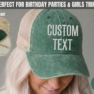 May include: A jade green trucker hat with a mesh back and white embroidered text that reads CUSTOM TEXT. The underside of the brim features a beige and white daisy floral pattern. The hat has a distressed finish and a structured front panel.
