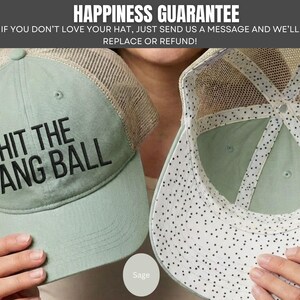 May include: A sage green trucker hat with a mesh back and the black embroidered text HIT THE DANG BALL on the front. The interior of the hat features a white lining with a black speckled pattern along the seams and the underside of the brim.