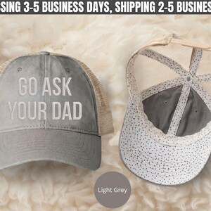 K&ouml;nnte beinhalten: Zwei hellgraue Trucker-Caps. Auf einer Kappe ist der Text "GO ASK YOUR DAD" wei&szlig; gestickt. Die andere Kappe ist nach innen gedreht und zeigt das Innendesign. Die Kappen haben einen Mesh-R&uuml;cken und einen gebogenen Schirm. Die Farbe der Kappe ist hellgrau.