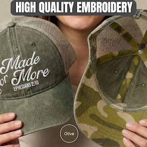 May include: An olive green trucker hat with a mesh back and white embroidered text that reads Made for More EPHESIANS 2:10. The interior of the hat features a camouflage pattern on the underside of the brim and along the inner structural seams.