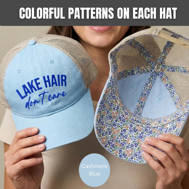 May include: Two light blue trucker hats with beige mesh backs. One hat features the dark blue text "LAKE HAIR don't care" on the front. The other hat is shown from the inside, revealing a floral pattern lining with blue and orange flowers.