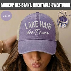 May include: A violet baseball cap with a mesh back and the embroidered white text "LAKE HAIR don't care" on the front. The cap features a makeup resistant, breathable sweatband and a rear opening with a floral patterned interior lining.