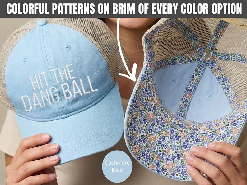 May include: A light blue trucker hat with a mesh back and the white embroidered text HIT THE DANG BALL on the front. The interior of the brim and the inner seams feature a colorful floral pattern with small blue and peach flowers on a white base.