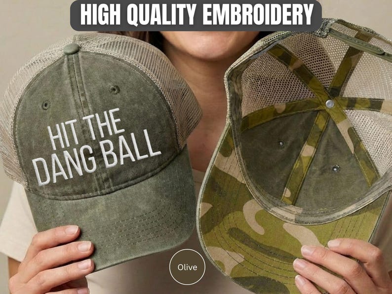 May include: An olive green trucker hat with a mesh back and the white embroidered text HIT THE DANG BALL on the front. The interior of the hat features a camouflage pattern on the underside of the brim and along the inner crown panels.
