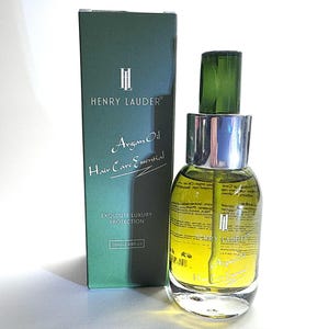 Puede incluir: Una caja verde con el texto "Henry Lauder" y "Argan Oil Hair Care Essential" en ella. La caja est&aacute; al lado de una botella de vidrio transparente con una tapa plateada y una parte superior verde. La botella contiene un l&iacute;quido amarillo y tiene el texto "Henry Lauder" en ella.