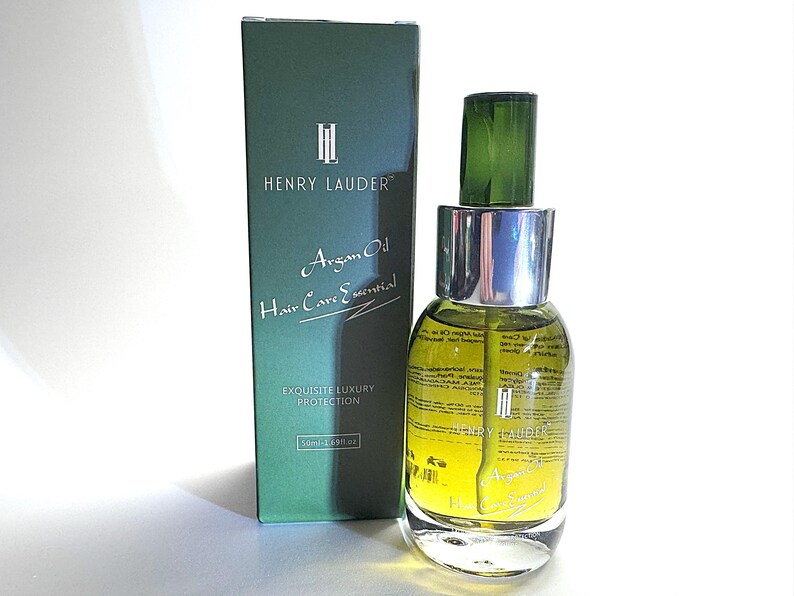 Puede incluir: Una caja verde con el texto "Henry Lauder" y "Argan Oil Hair Care Essential" en ella. La caja est&aacute; al lado de una botella de vidrio transparente con una tapa plateada y una parte superior verde. La botella contiene un l&iacute;quido amarillo y tiene el texto "Henry Lauder" en ella.
