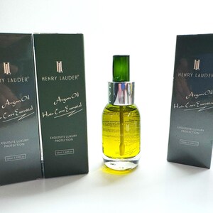 Puede incluir: Tres botellas de aceite de arg&aacute;n para el cuidado esencial del cabello con el nombre de la marca Henry Lauder impreso en la parte delantera. Las botellas son verdes y tienen una etiqueta dorada con texto blanco. El texto de la etiqueta dice "Argan Oil Hair Care Essential" y "Exquisite Luxury Protection".