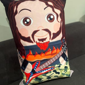 May include: A rectangular decorative pillow featuring a cartoon illustration of a man with brown hair and a beard. The man is wearing a shirt with a guitar and flames design. The pillow has a camouflage pattern on the bottom.