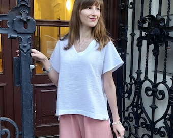 May include: A woman wearing a white, short-sleeved, v-neck top with pink, wide-leg trousers and a gold handbag.