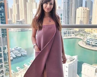 May include: A woman wearing a mauve waffle weave linen wrap dress with a side slit and a pocket. The dress is made of 100% linen and is perfect for lounging around the house or running errands.