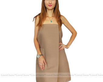 May include: A brown waffle weave wrap style towel with a pocket. The towel is worn by a person and is shown from the front.