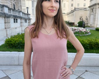May include: A woman wearing a pink sleeveless top and matching pants. The top has a scoop neck and the pants are wide-legged. She is standing in front of a building with a garden.