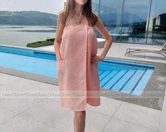 May include: A pink waffle weave bathrobe with a wrap style closure and a pocket on the side. The robe is worn by a person standing near a swimming pool.