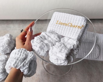 May include: Set of white waffle weave fabric hair scrunchies and a headband with the text "Linen Charm" embroidered in gold thread.