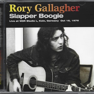 May include: CD case for Rory Gallagher's album "Slapper Boogie." The cover features a black background with the album title and artist's name in yellow and red. A black and white photo of a man playing an acoustic guitar is in the center.
