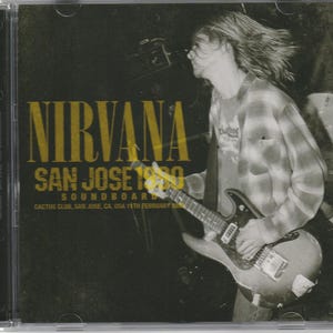 May include: A Nirvana San Jose 1990 Soundboard CD case featuring a black and white photograph of a musician playing an electric guitar. The cover includes gold text reading Nirvana, San Jose 1990, Soundboard, and Cactus Club, San Jose, CA, 11th February 1990.