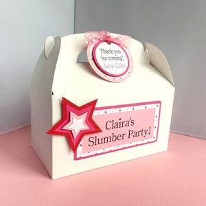 May include: White favor box with a pink and white polka dot ribbon, a pink and white star, and a pink tag that says "Thank you for coming! Love, Clair." The box also has a pink and white label that says "Clair's Slumber Party!"
