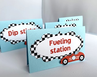 Könnte beinhalten: Vier blaue und weiße Lebensmitteletiketten mit einem karierten Rand und einem weißen Oval in der Mitte. Die Etiketten lauten "Dip Sticks", "Fueling Station" und zwei weitere Etiketten, die nicht sichtbar sind. Die Etiketten haben ein rotes Rennwagen mit einer weißen Nummer 2 an der Seite.