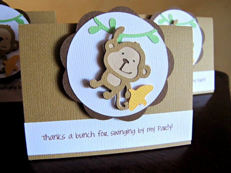 May include: Brown and white thank you card with a brown monkey hanging from a green vine. The monkey is holding a yellow star. The card says "thanks a bunch for swinging by my party!"