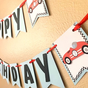 May include: A blue and white banner with the words "Happy Birthday" in black letters. The banner is decorated with red race cars and black and white checkered flags.