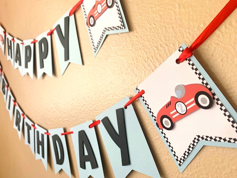 May include: A blue and white banner with the words "Happy Birthday" in black letters. The banner is decorated with red race cars and black and white checkered flags.