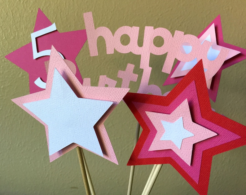 May include: Pink and red layered paper stars with a white star in the centre. The stars are on sticks and have the words "happy birthday" in pink paper letters.