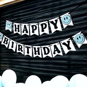 May include: White banner with black letters spelling "Happy Birthday" with blue and white smiley faces with lightning bolts on each end.