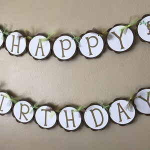 May include: A brown and white banner with the words "Happy Birthday" decorated with green leaves and small monkeys. The banner is strung with twine and has brown scalloped edges.