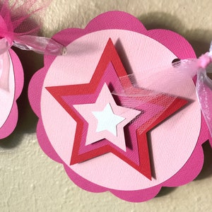 May include: Pink and red paper star banner with pink tulle ribbon. The banner is made of scalloped circles with a star in the center.